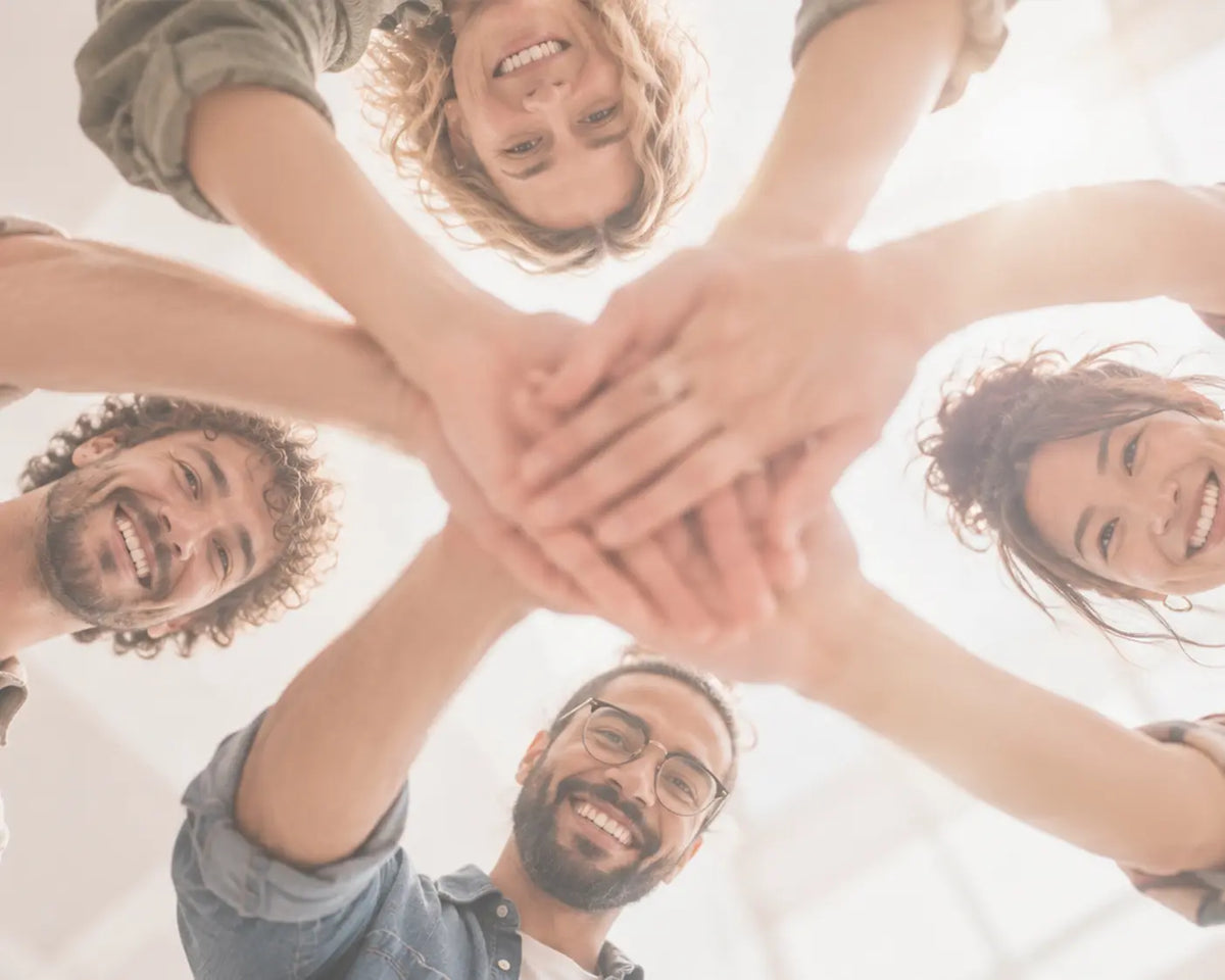 AZIKX Teamwork und Zusammenhalt – vier kreative Menschen legen gemeinsam ihre Hände übereinander