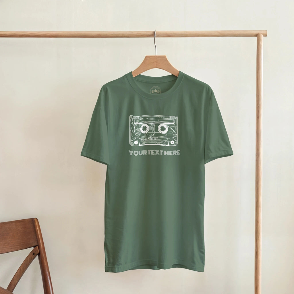 Olive green T-shirt with a retro cassette and sample text “YOUR TEXT HERE”, front view.